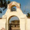 A historic adobe archway with a bell and gated entrance.