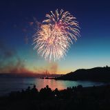 Fireworks lighting up the sky above a beach at sunset.