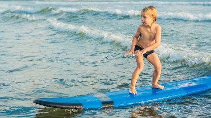 Young boy balancing on a surfboard in shallow ocean waves.