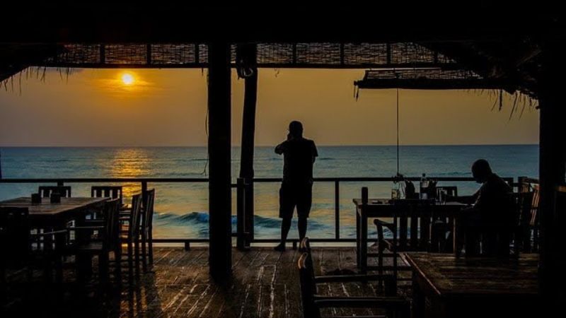 Silhouette of a person photographing the ocean at sunset from a beachfront restaurant.