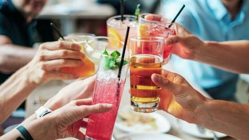 Group of people clinking colorful cocktails together.